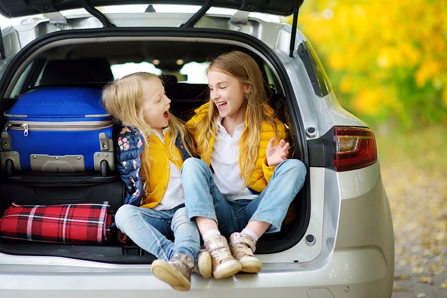 Personal Insurance - Two Young Girls Sitting in the Back of a Car with a Suitcase Getting Ready to go Camping with Their Parents