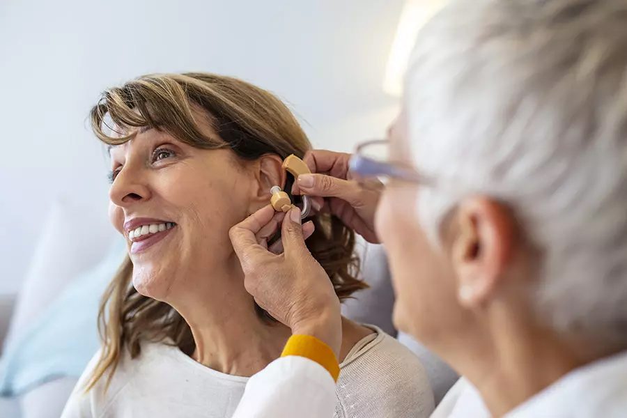 Dental Vision and Hearing Plans - Doctor Adjusting Hearing Aid of a Senior Patient in Her Office